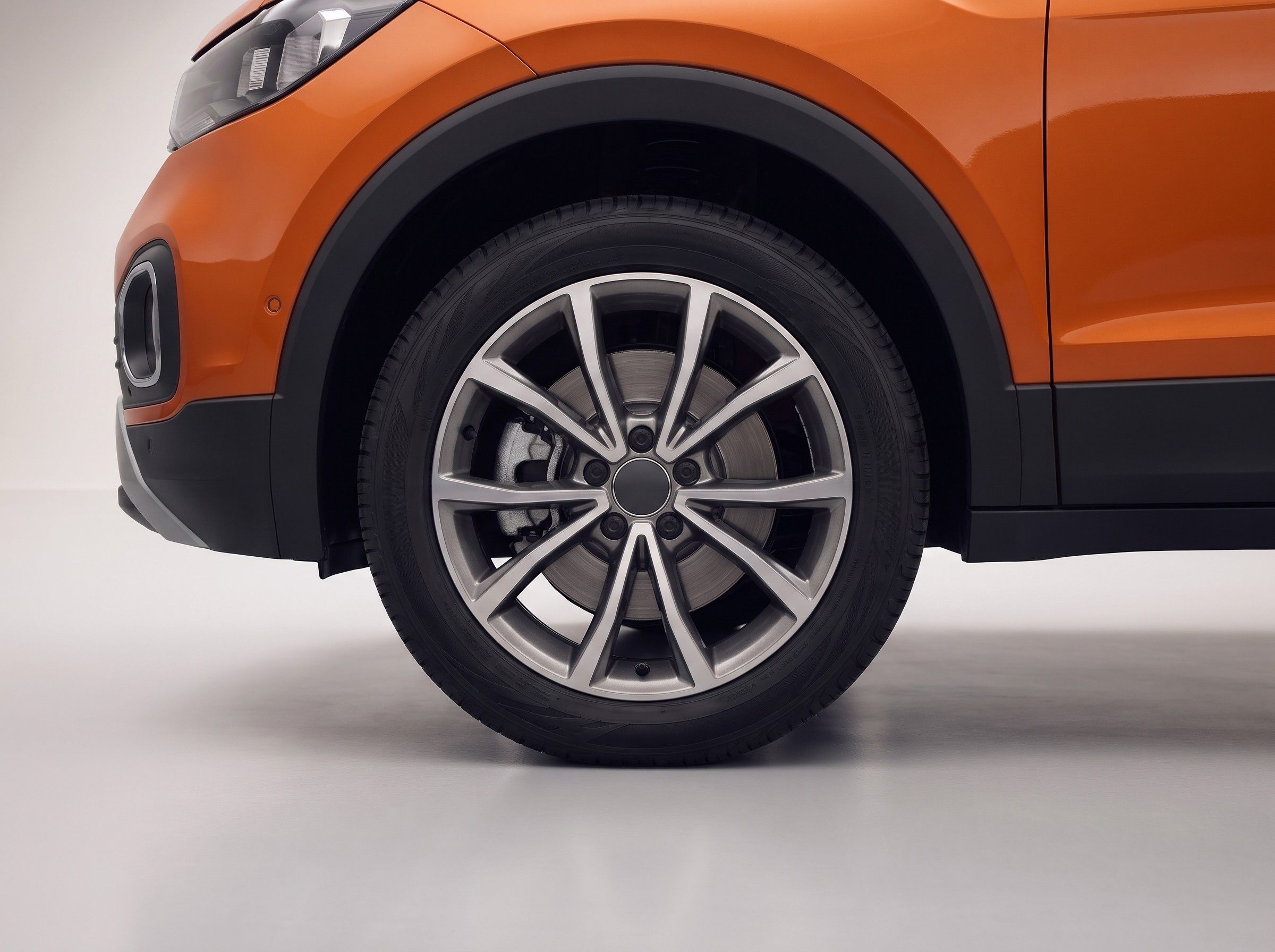 Detalhe da roda dianteira de um SUV laranja, com o disco e a pinça de freio aparentes.